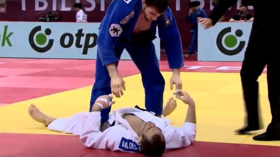 Un judoka blessé étendu au sol. Son adversaire tente de l'aider