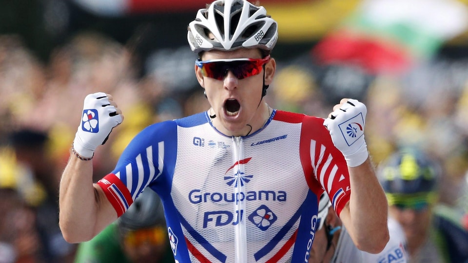 Un cycliste casqué crie, lève les bras et serre les poings pour célébrer sa victoire.