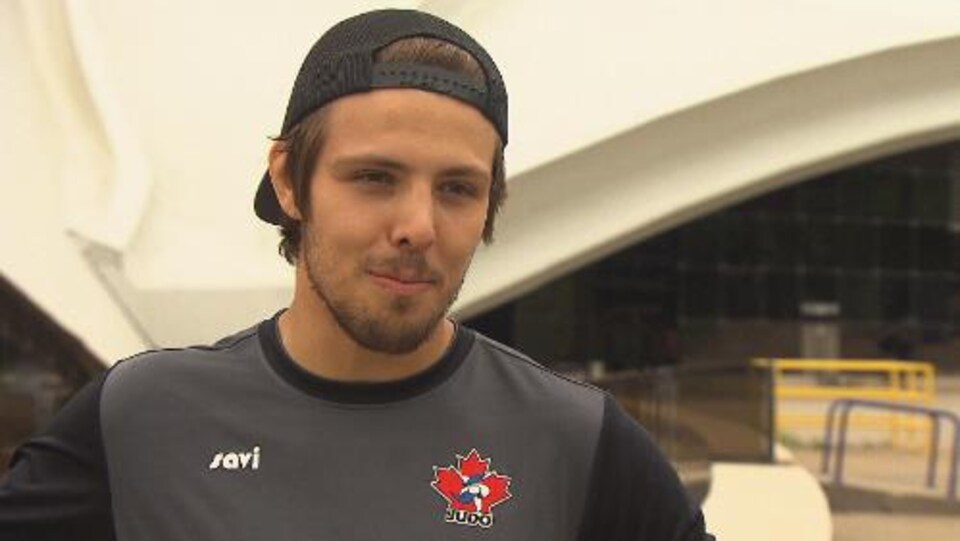 Un athlète avec une casquette et un chandail gris de Judo Canada donne une entrevue.