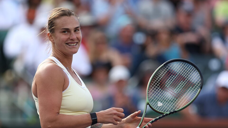 Une joueuse de tennis tient sa raquette dans une main et sourit après avoir remporté un match.