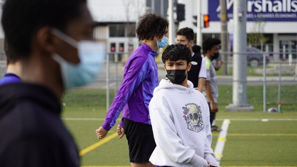 Plusieurs jeunes joueurs de soccer attendent sur une ligne le commencement d'un exercice avec un couvre-visage.