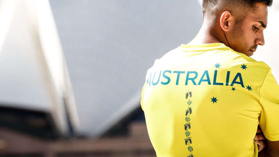Il pose de dos et regarde de côté devant l'Opéra de Sydney.
