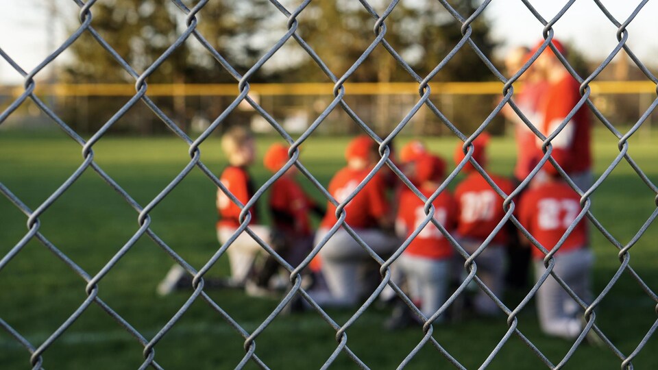 Des jeunes agenouillés sur le terrain de baseball regardent leurs entraîneurs.
