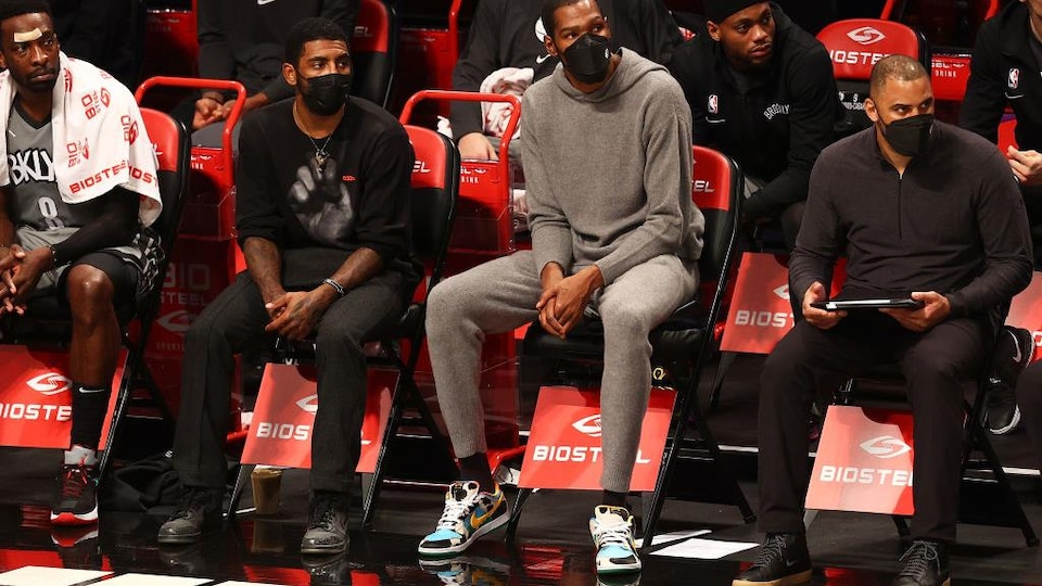 Il est assis à côté de son coéquipier Kevin Durant au banc. Ils portent un masque.