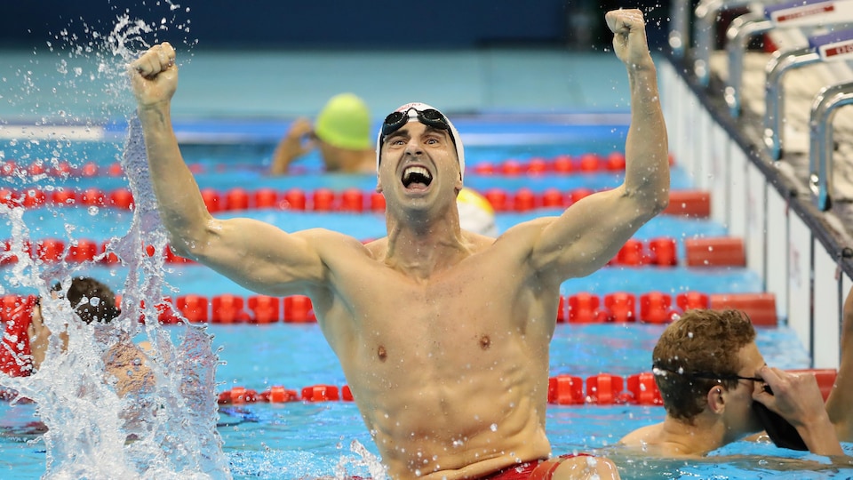 Un nageur lève les bras en triomphe dans son couloir après sa course.