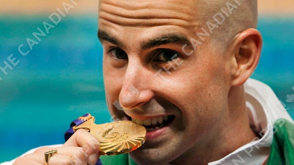 Benoit Huot croque sa médaille d'or sur le podium des Jeux du Commonwealth de 2010 à New Delhi