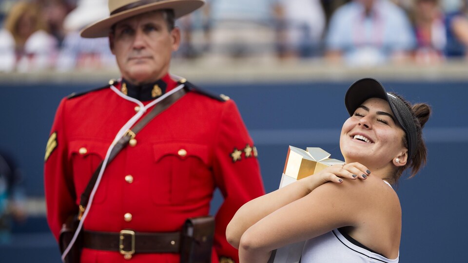 Elle serre entre ses bras le trophée de la Coupe Rogers devant un agent de la GRC.