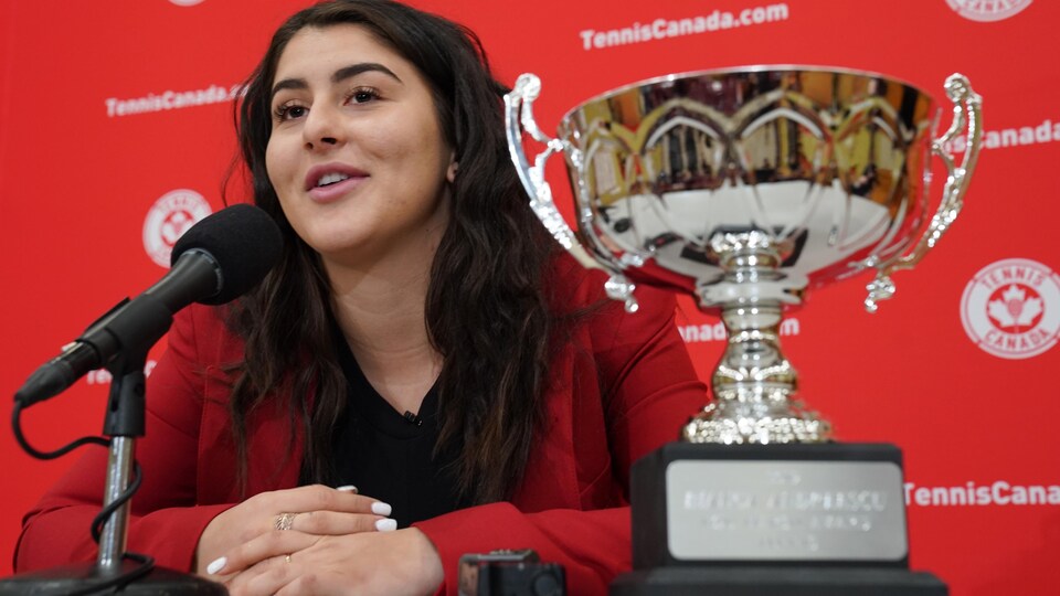 Elle donne une conférence de presse avec le trophée à sa gauche.