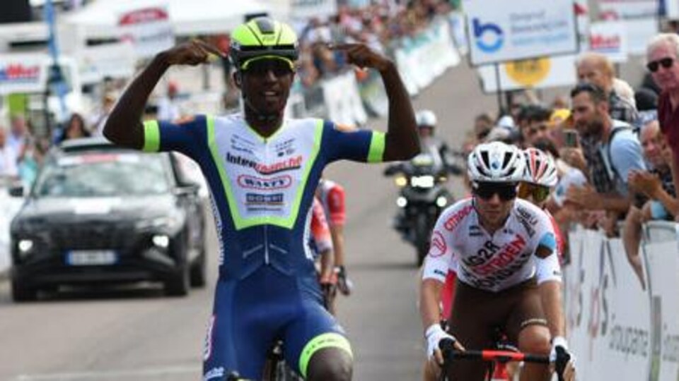 One cyclist raises his arms while crossing the finish line in front of another.