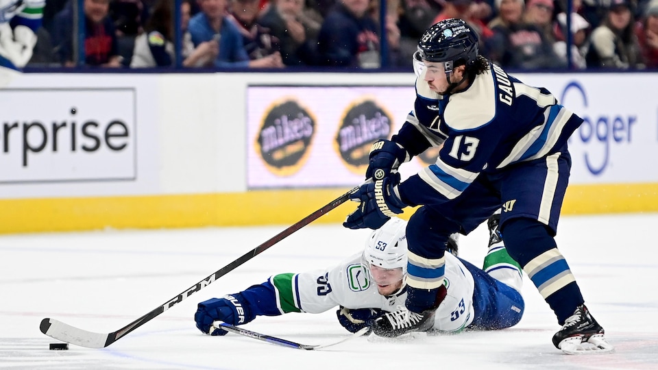 Un joueur de hockey est allongé sur la glace et un autre est debout sur ses patins.