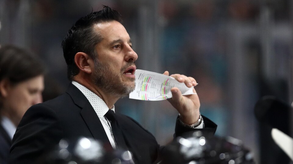 Un entraîneur de hockey, derrière le banc des joueurs, donne des instructions.