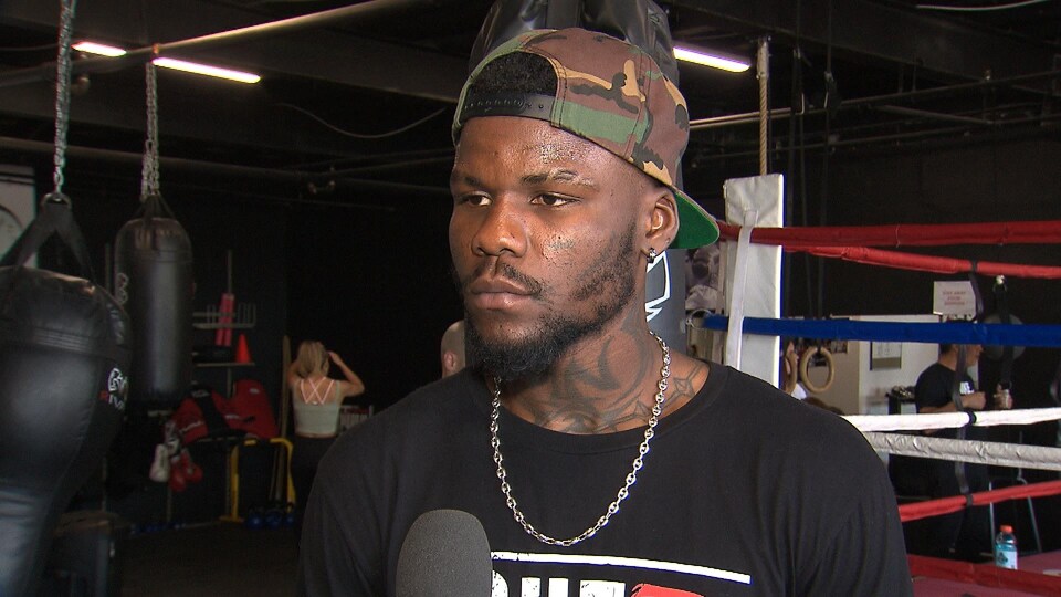 A boxer in black gives a lecture near a ring.
