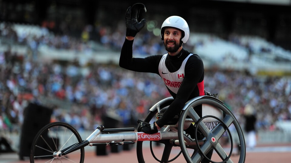 Assis dans son fauteuil roulant, il lève le bras droit.