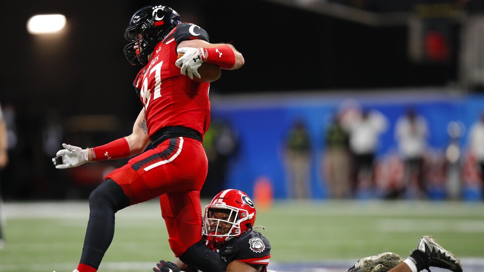 Un joueur de football vêtu de rouge se fait saisir la jambe par un rival lors d'un match de la NCAA.