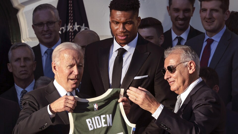 Il tient un chandail des Bucks de Milwaukee, entouré de plusieurs autres hommes.