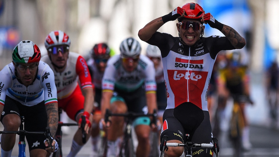 Le cycliste pose les mains sur son casque et sourit en franchissant l'arrivée.