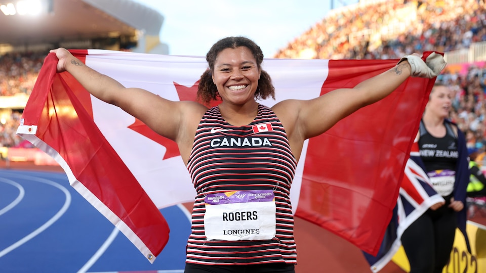 Une athlète sourit en brandissant fièrement le drapeau canadien.