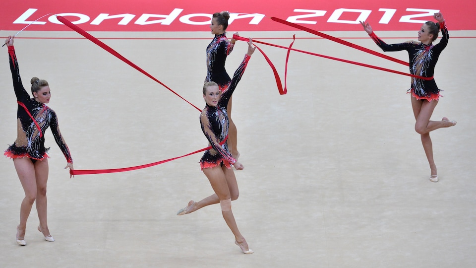 Quatre gymnastes font des figures avec des rubans rouges.