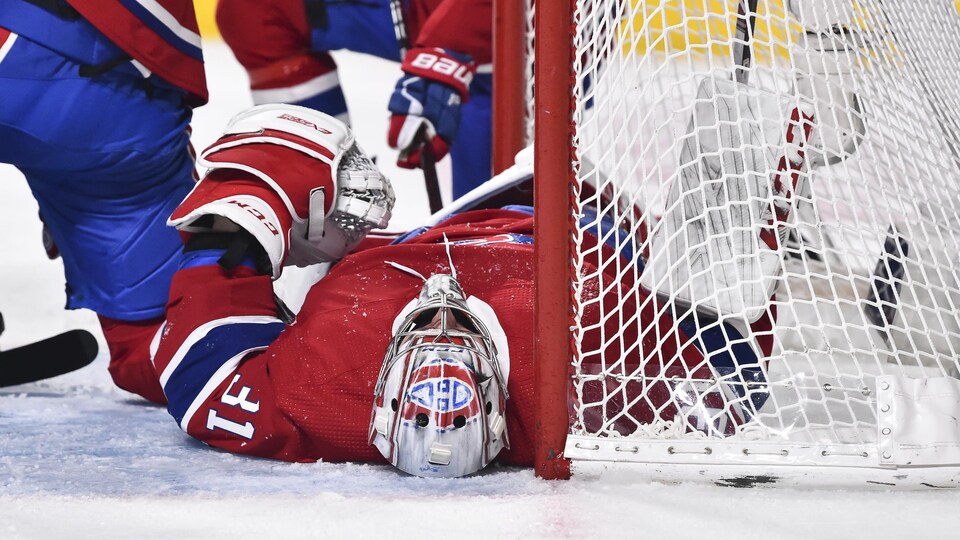 Il est couché dos sur la patinoire devant son filet.
