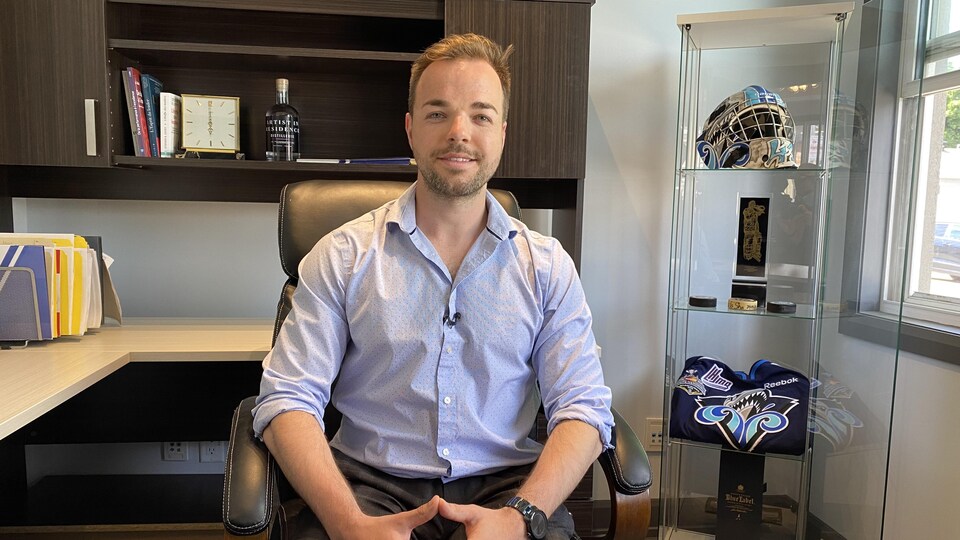 Carl Hozjan pose dans son bureau. Près de lui, des souvenirs datant de son parcours de gardien de but dans la LHJMQ.