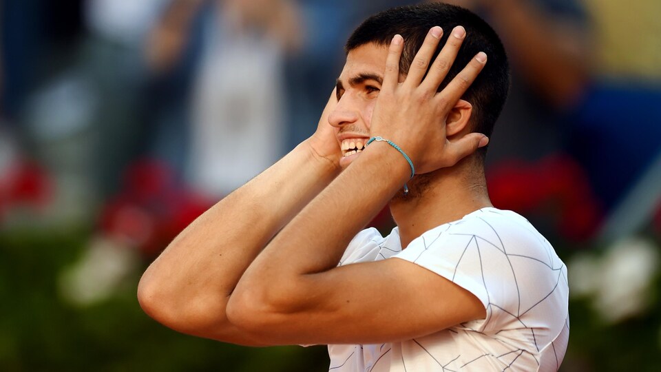 Un joueur de tennis sourit et se tient la tête entre les mains.