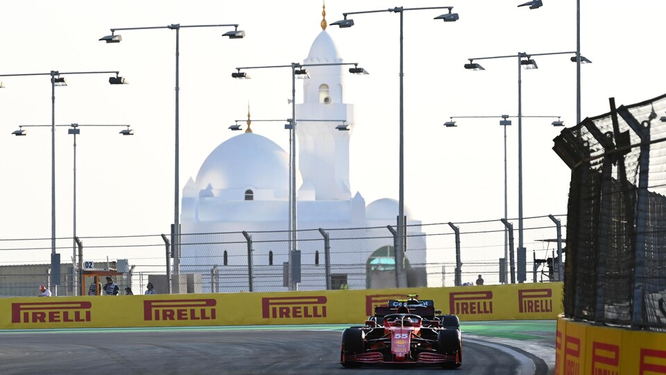 Two F1 cars drive on a circuit surrounded by low walls and security fences.