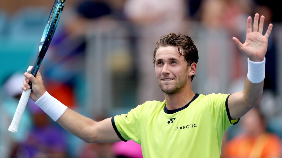 Le joueur de tennis lève ses bras dans les airs, avec sa raquette dans la main droite, après sa victoire.