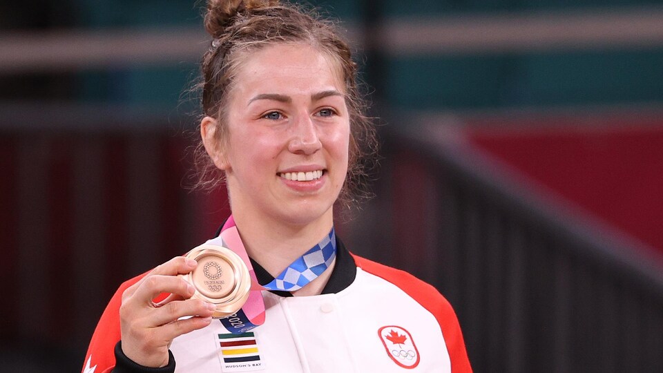 Une athlète souriante tient de la main droite une médaille de bronze.