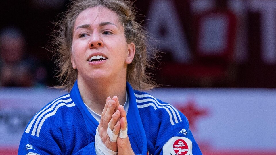 Une judoka sourit et joint les mains en signe de victoire.