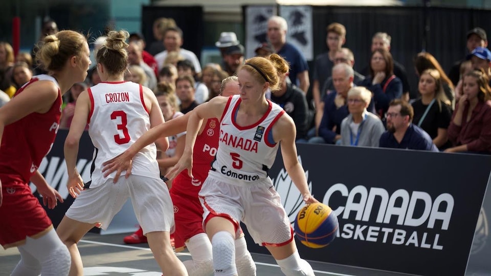 Une joueuse de basketball protège son ballon pendant un match devant les yeux de spectateurs attentifs.
