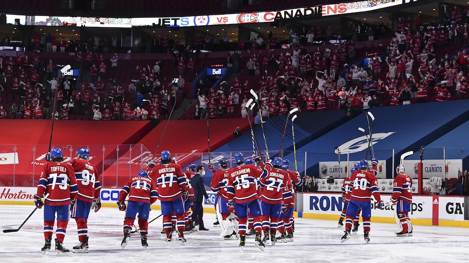 Les joueurs sur la glace saluent la foule en levant leurs bâtons dans les airs.