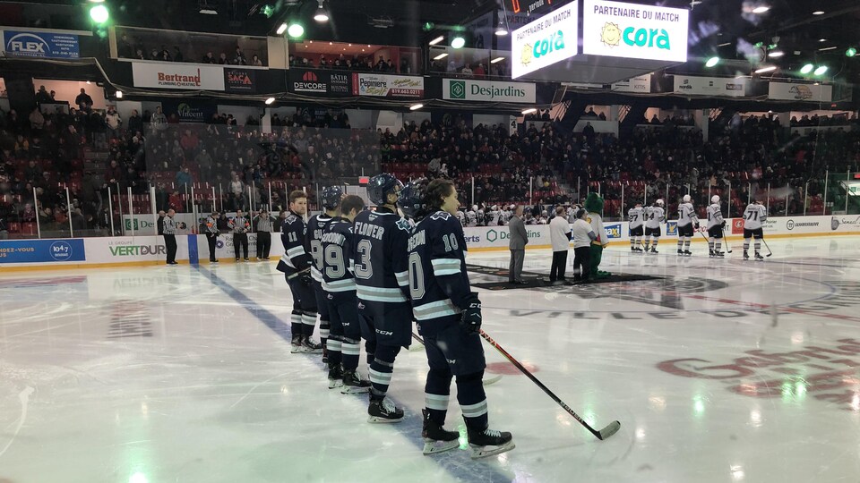 Quatre joueurs de hockey se tiennent debout sur leurs patins au centre de la glace.