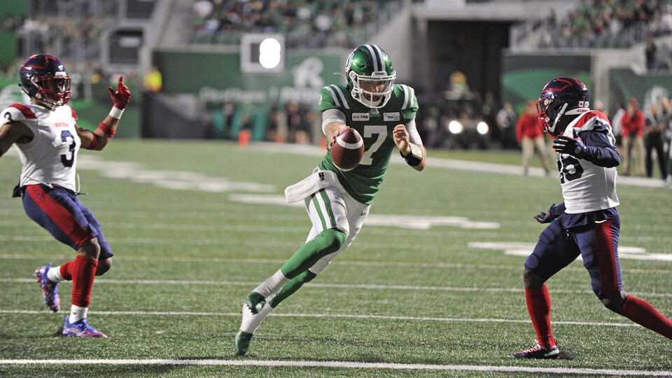 Le joueur de football Cody Fajardo se fraie un chemin vers la zone des buts, passant entre deux adversaires des Alouettes.