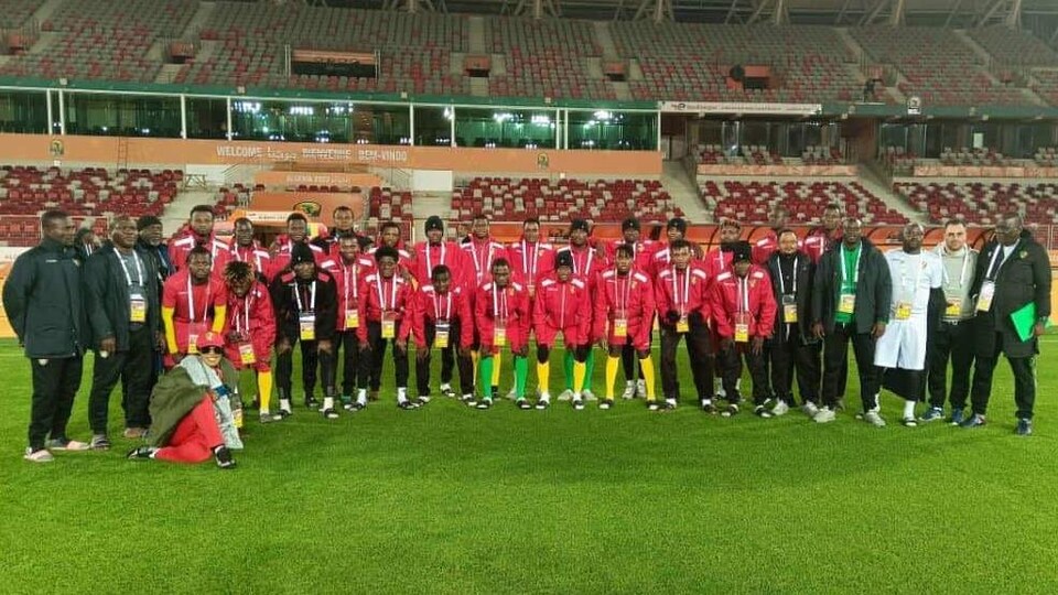 équipes de joueurs et d'entraineurs portant du rouge sur le terrain pour une photo de groupe avec en arrière-plan des estrades