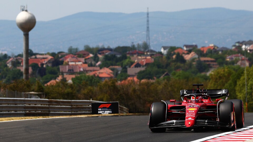 Une monoplace de Ferrari roule sur le circuit de Budapest, on voit un château d'eau en arrière-plan et des toits de maison.