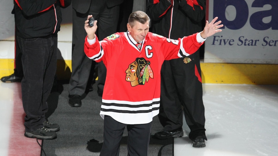 Un homme, qui porte un chandail des Blackhawks de Chicago, lève les bras au centre de la glace.