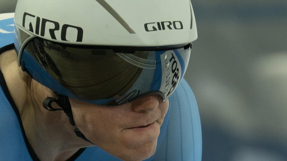 Le cycliste canadien, dans un maillot bleu et un casque blanc aérodynamique, regarde la piste avant sa course. 