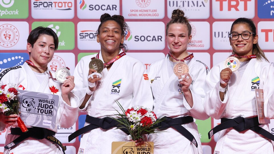 Quatre judokas montrent leurs médailles pour la photo sur un podium. 