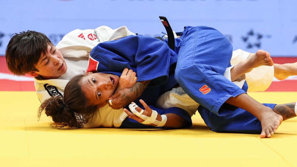 Deux judokates en plein combat sont au sol sur le tatami.