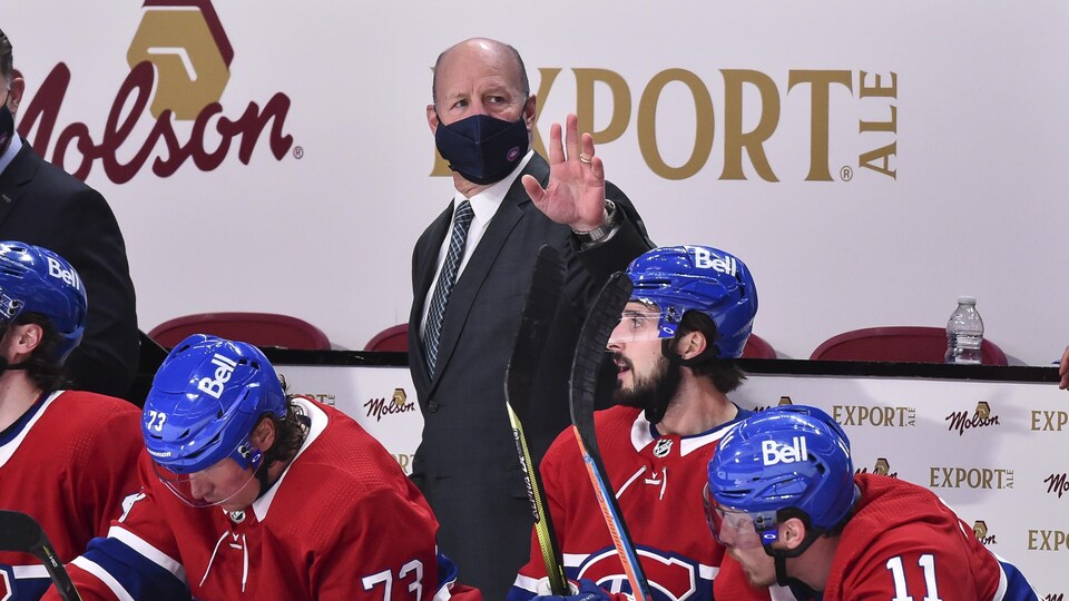 Il est debout derrière le banc des joueurs.