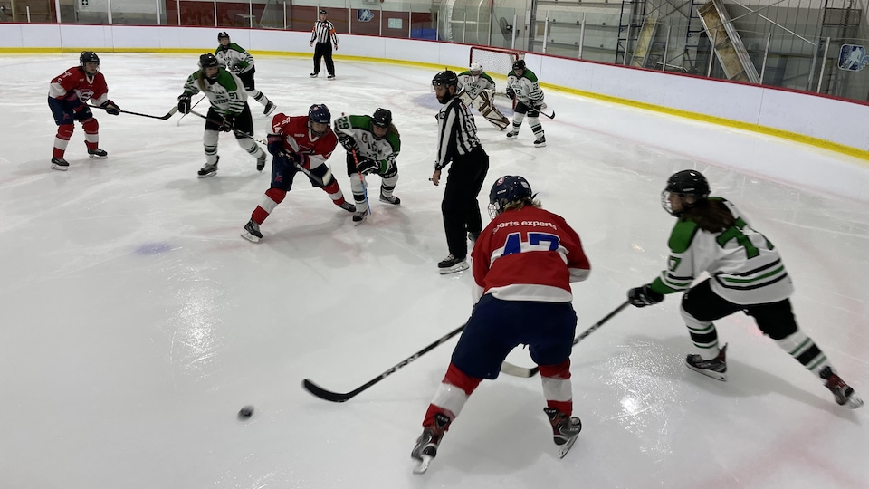 Des joueuses de hockey s'affrontent pendant un match. Une équipe porte un uniforme blanc et vert et l'autre du rouge.