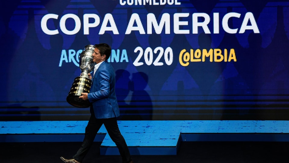 Il transporte le trophée sur une scène où est affichée le logo de la Copa América.
