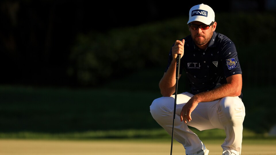 Corey Conners, accroupi, regarde le terrain de golf.