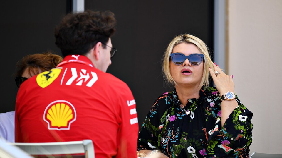 Une femme avec des lunettes de soleil discute avec un homme en combinaison rouge.