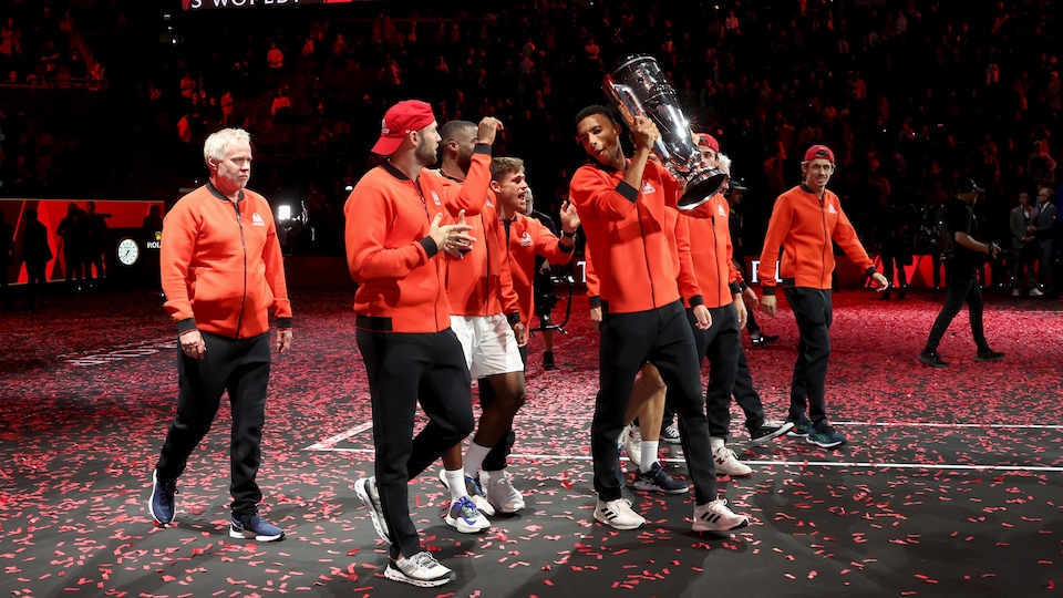 Le joueur de tennis canadien, en rouge, soulève l'imposant trophée, entouré de son équipe. 