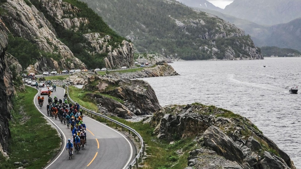 Un peloton suit une route sinueuse le long d'un fjord. 