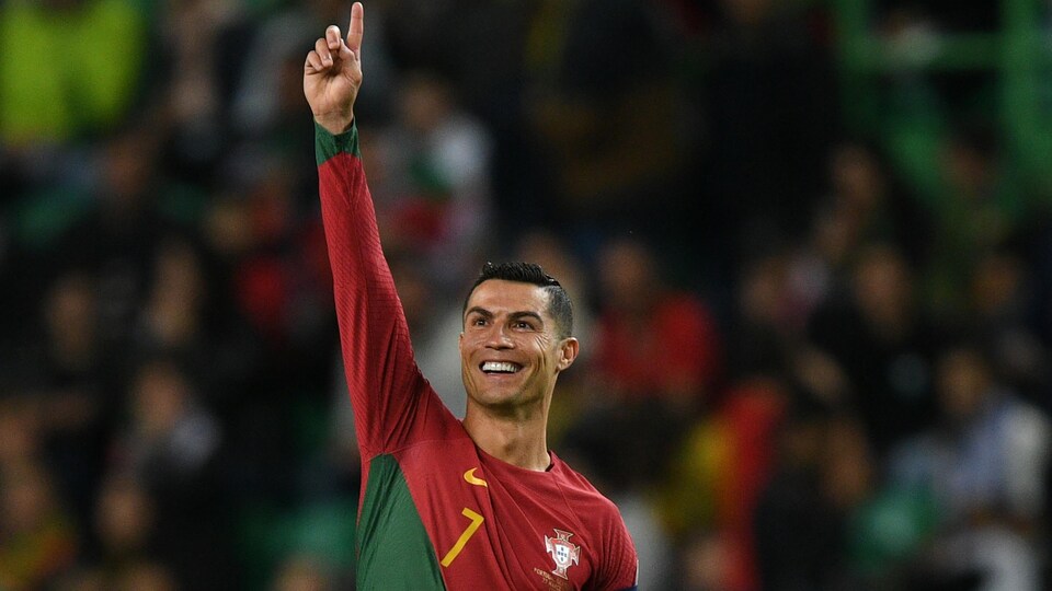 Un joueur de soccer, tout sourire, lève le bras droit pour saluer la foule.