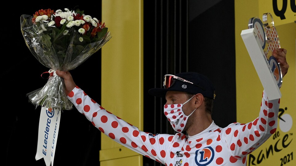 Il soulève son trophée et un bouquet de fleurs sur le podium.