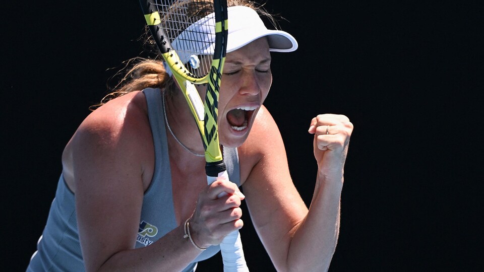 Une joueuse de tennis, avec une casquette, crie après un point, sa raquette dans la main droite.