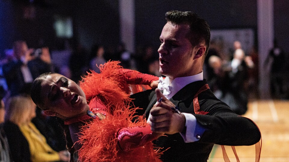 Un danseur en complet noir avec sa partenaire en rouge.